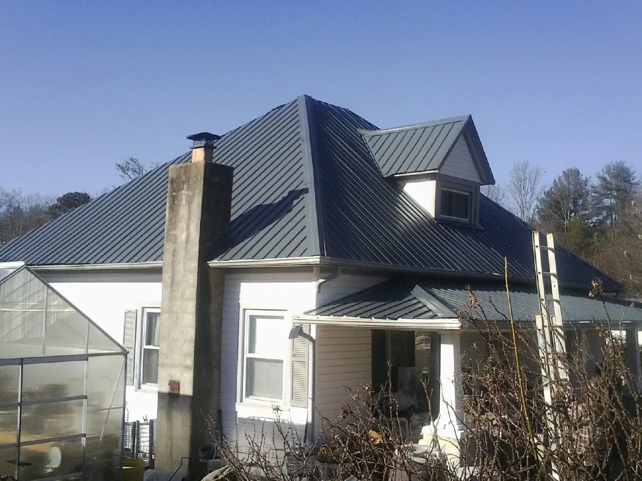 Dark blue standing seam metal roof on a white farmhouse with dormer — Slate & Tile Roof Repair by Roofing Brothers in Clark