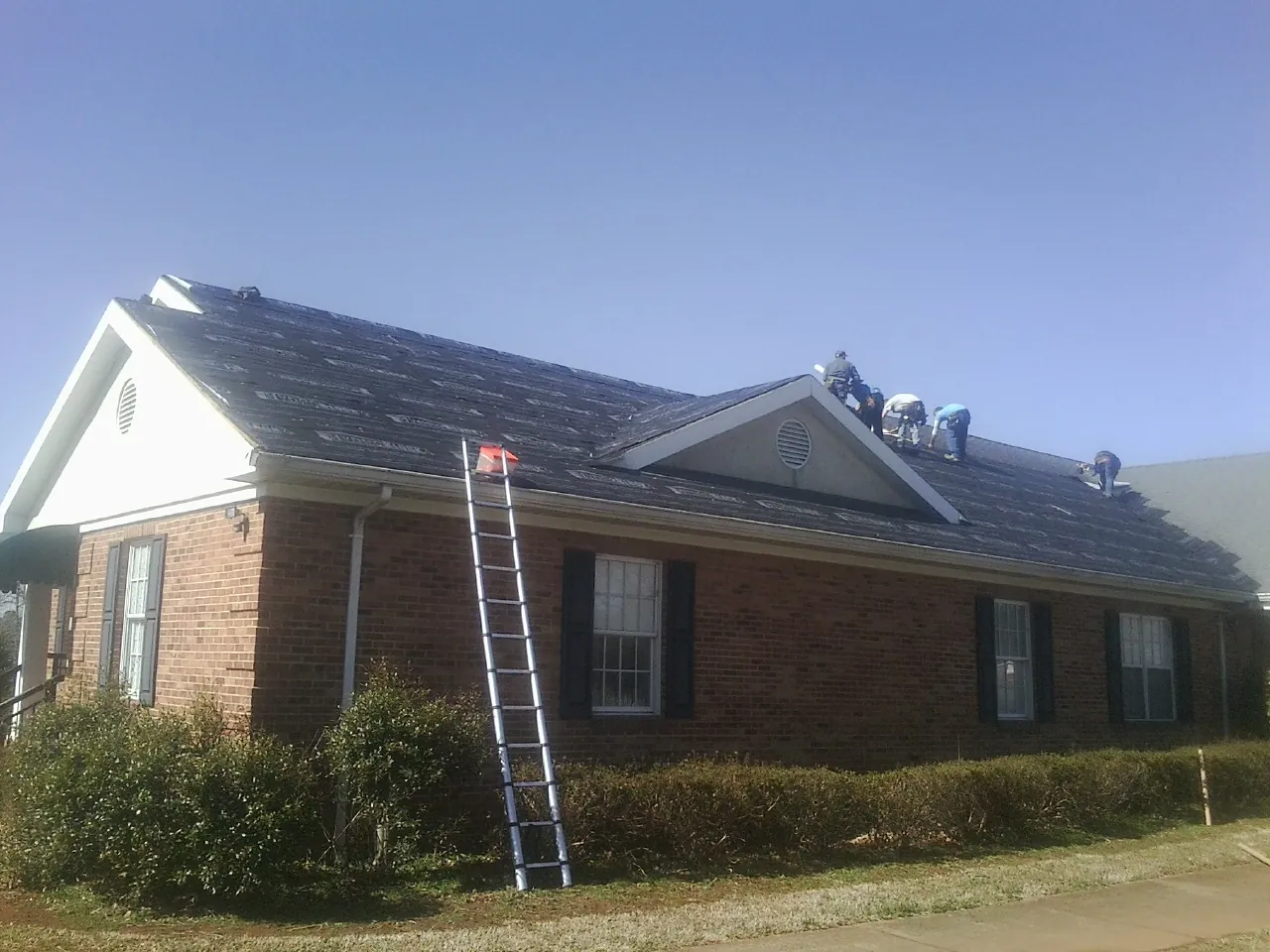 Crew tearing shingles off a brick ranch roof with a ladder set — Emergency Roof Repair work by our crew in Clark