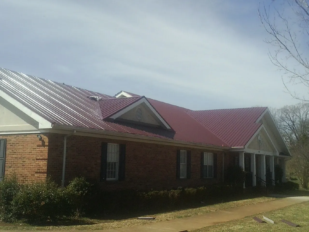 Red metal roof with gabled entries on a long brick building, from a Hail Damage Roof Repair job in Clark