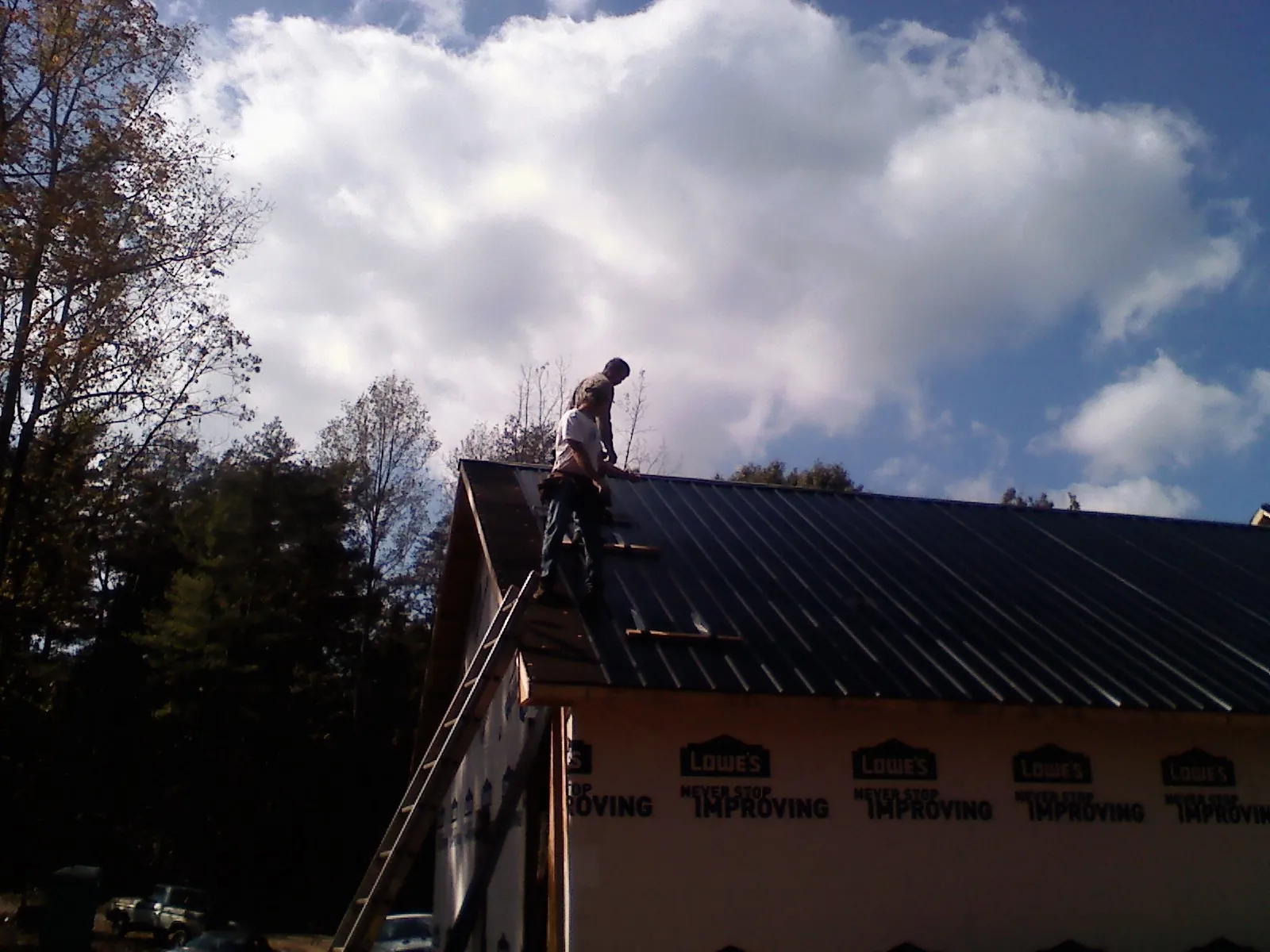 Roofer fastening dark metal panels high against a cloudy sky, from a Roof Inspection job in Clark