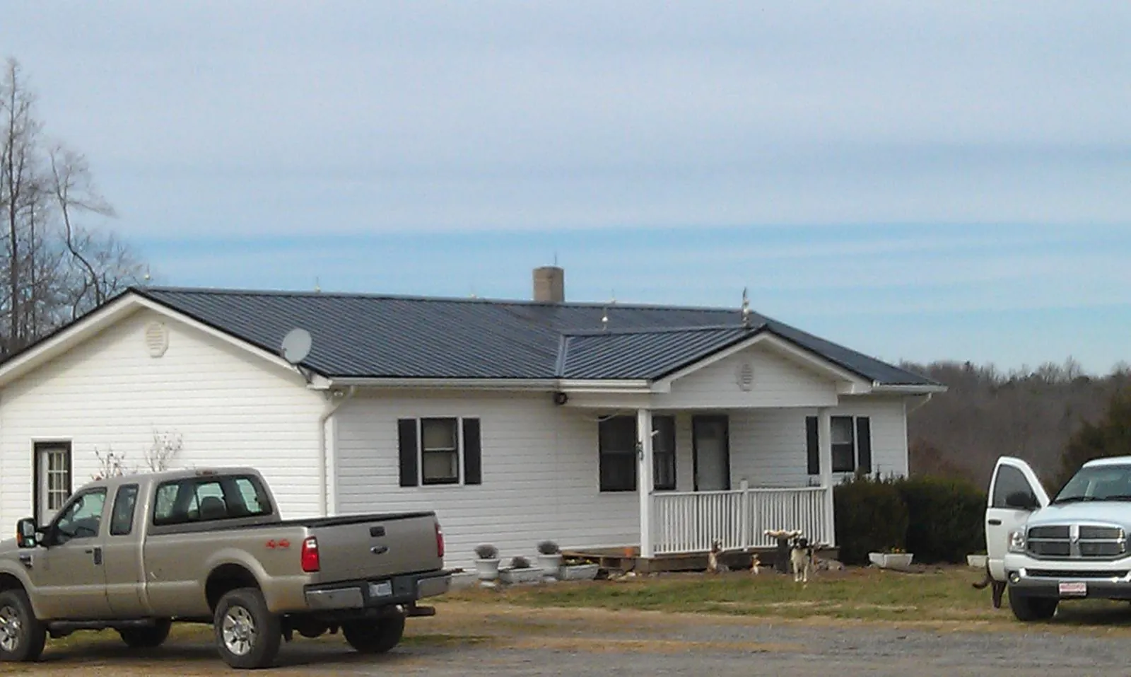 Finished dark metal roof on a white ranch home with work trucks parked in Clark